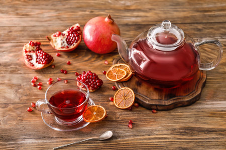 Teapot and cup of tasty pomegranate juice on wooden tableの写真素材