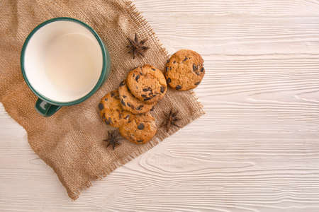 Tasty cookies with chocolate chips and cup of milk on light wooden table