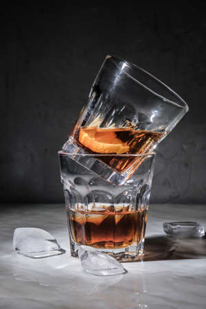 Glasses of whiskey and ice cubes on table