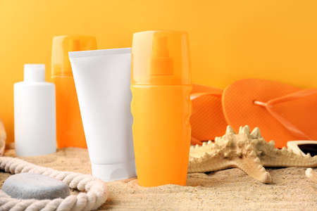 Different sun protection creams on sand against color background