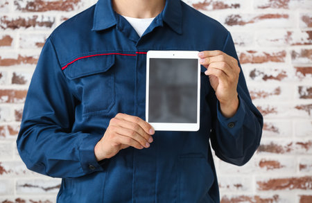 Male car mechanic with tablet computer near brick wall, closeupの写真素材
