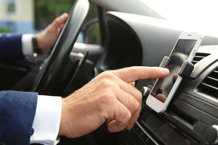 Businessman using mobile phone for navigation while driving car, closeup