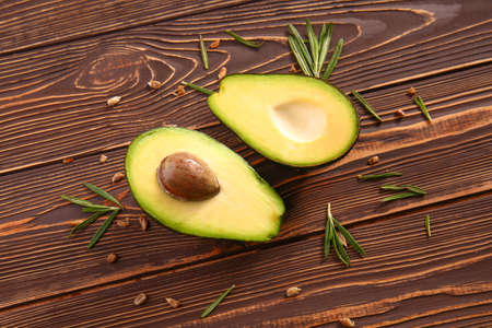 Halves of raw avocado with rosemary and seeds on wooden table