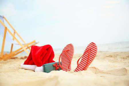 Santa Claus hat with gift box and flip-flops on sea coast. Christmas vacationの写真素材