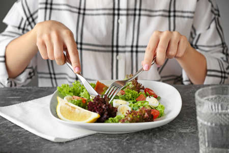 Woman eating tasty salad at table, closeup