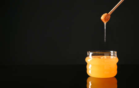 Jar and dipper with tasty honey on dark background