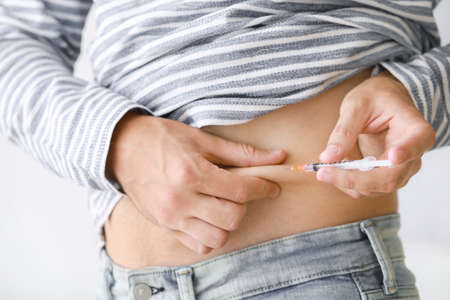 Diabetic man giving himself insulin injection at home, closeup