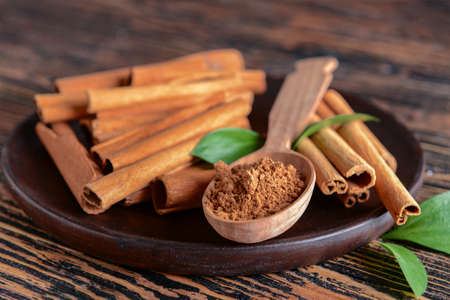 Plate with aromatic cinnamon sticks and powder on wooden background, closeupの写真素材