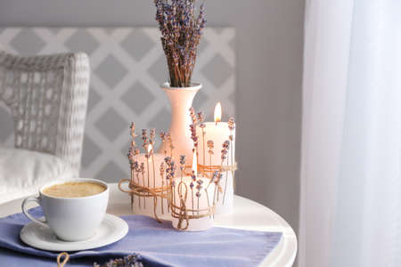 Cup of coffee, burning candles and lavender on table in room