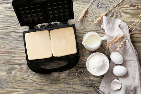 Modern waffle maker with ingredients on wooden table