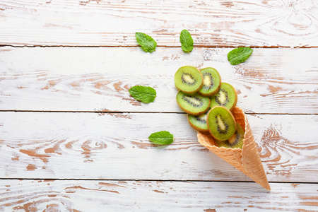 Tasty ripe kiwi in waffle cone on wooden backgroundの写真素材
