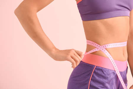 Beautiful young woman with measuring tape on color background, closeup. Weight loss concept