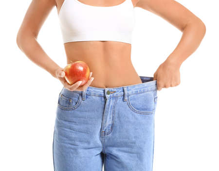 Beautiful young woman in loose jeans and with apple on white background. Weight loss conceptの写真素材