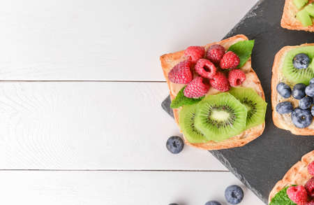 Slate plate with tasty sandwiches, kiwi and berries on white tableの写真素材
