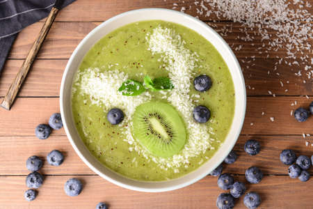 Bowl with tasty kiwi smoothie and blueberry on wooden table