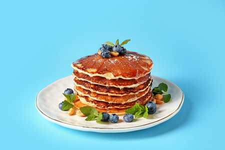 Plate with tasty pancakes and blueberries on color background