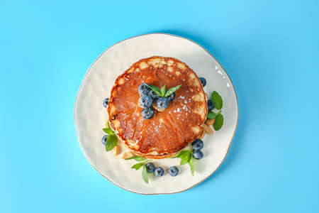 Plate with tasty pancakes and blueberries on color background
