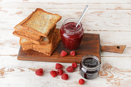 Board with tasty toasted bread and different jams on white table