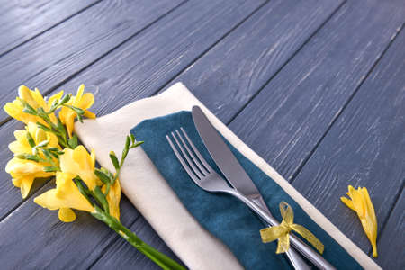Cutlery, napkin and flowers on wooden background, closeup