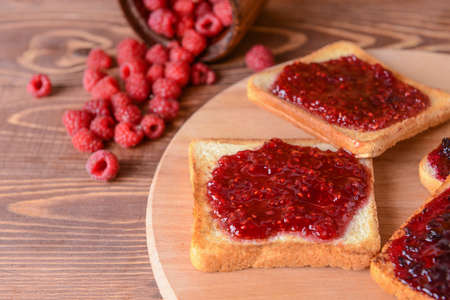 Tasty toasted bread and raspberry jam on wooden board
