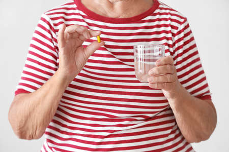 Elderly woman with pill and glass of water on light background, closeupの写真素材