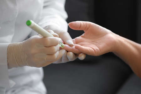 Doctor taking blood sample of diabetic woman at home, closeup