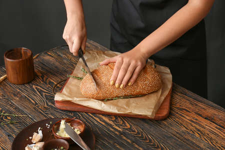 Woman cutting fresh bread at table, closeup