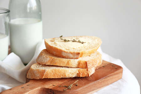 Slices of fresh bread with butter, herbs and milk on table