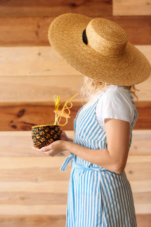 Woman with tasty Pina Colada cocktail in pineapple on wooden backgroundの写真素材