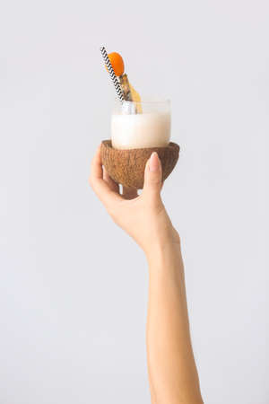 Female hand with tasty Pina Colada cocktail on light backgroundの写真素材