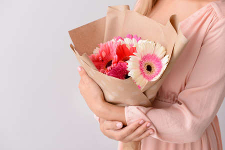 Woman with bouquet of beautiful gerbera flowers on light backgroundの写真素材