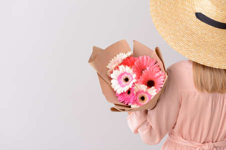 Woman with bouquet of beautiful gerbera flowers on light backgroundの写真素材