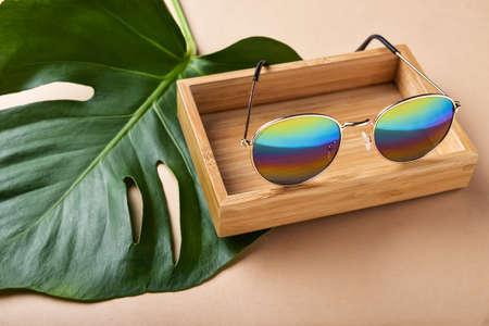 Box with stylish sunglasses and tropical leaf on color backgroundの写真素材