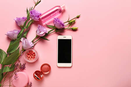 Modern mobile phone with makeup cosmetics and flowers on color backgroundの写真素材