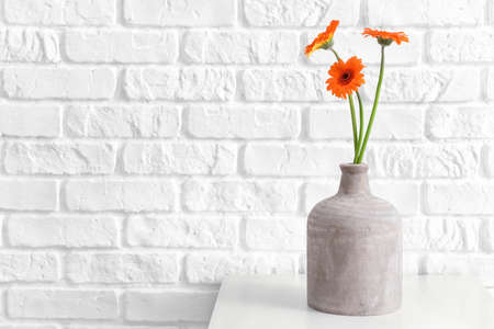 Vase with beautiful gerbera flowers on table near white brick wallの写真素材