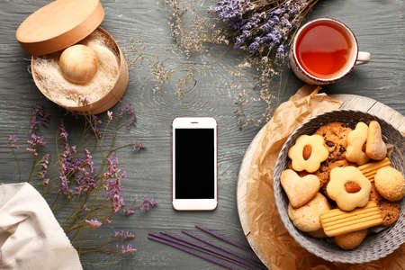 Modern mobile phone with cookies and cup of tea on wooden backgroundの写真素材