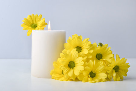 Burning candle with fresh flowers on light backgroundの写真素材