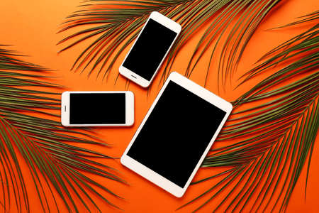 Modern tablet computer with mobile phones and tropical leaves on color backgroundの写真素材