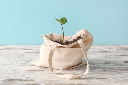 Eco bag with soil and plant on wooden table against color backgroundの写真素材