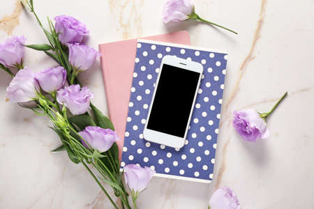 Mobile phone, notebooks and flowers on table