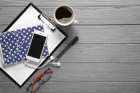 Composition with mobile phone, clipboard, notebook and cup of coffee on wooden background