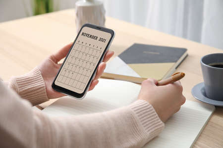 Woman with mobile phone using calendar application at tableの写真素材