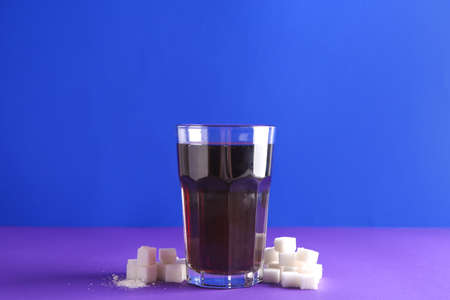 Glass of fresh cola and sugar on color background