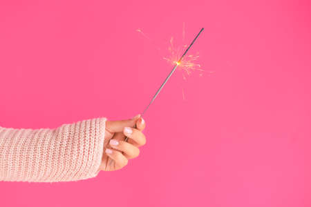 Female hand with festive Christmas sparkler on color background