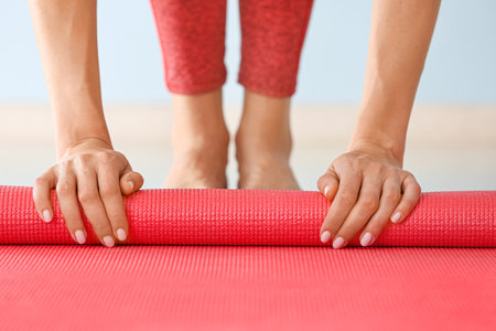 Young woman rolling yoga mat in gym, closeupの写真素材