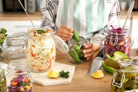 Woman preparing cucumbers for fermentation at table, closeup