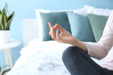 Young woman meditating on bed at home, closeup