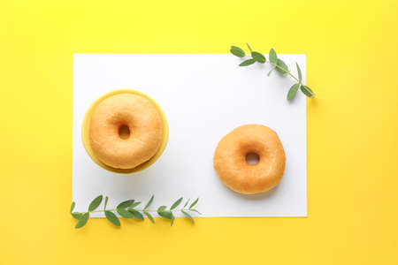 Sweet tasty donuts and blank paper sheet on color background