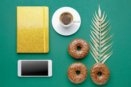 Composition with sweet tasty donuts, notebook, mobile phone and cup of coffee on color backgroundの写真素材