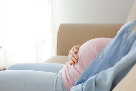 Beautiful pregnant woman sitting on sofa at homeの写真素材